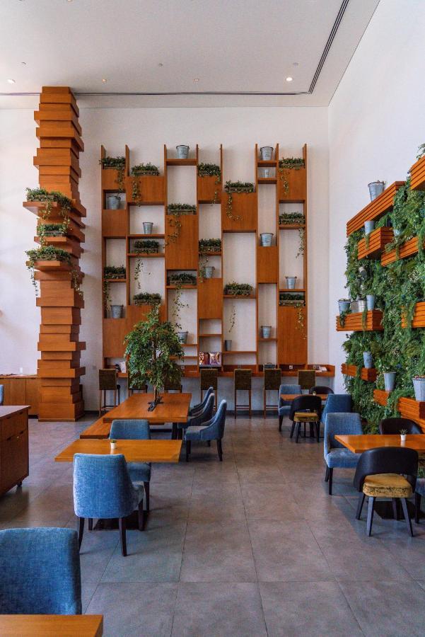 Canal Central Hotel Business Bay Dubaj Zewnętrze zdjęcie The photo shows a modern café or restaurant interior. There is a striking wooden wall featuring a series of shelves filled with potted plants, creating a lush green backdrop. On one side, there is a tall, vertical wooden structure that adds architect