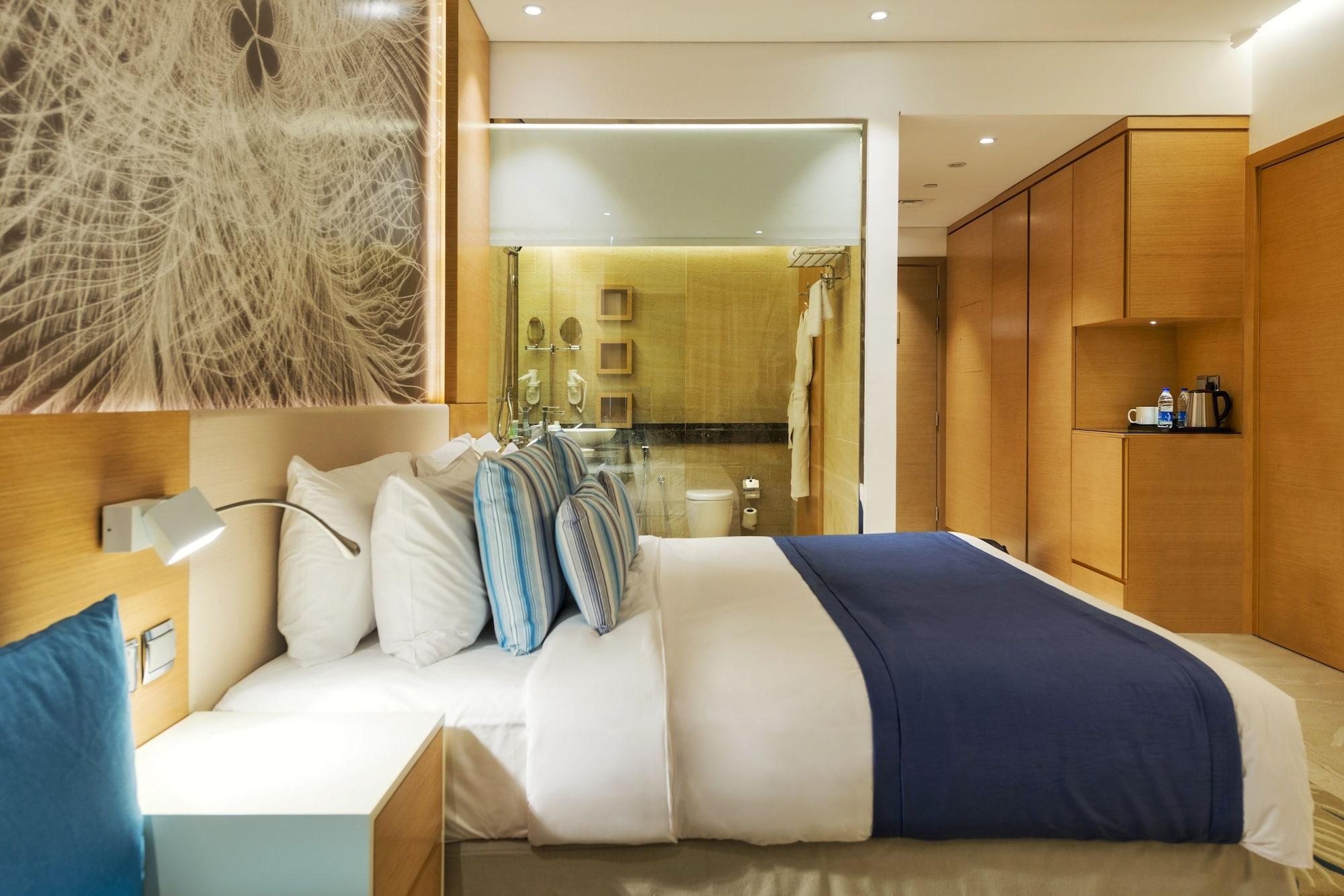 Canal Central Hotel Business Bay Dubaj Zewnętrze zdjęcie The photo shows a modern hotel room featuring a neatly made bed with white linens and decorative blue pillows. The walls are adorned with wooden paneling, and there is a large piece of artwork above the bed. On the right side of the room, there are b