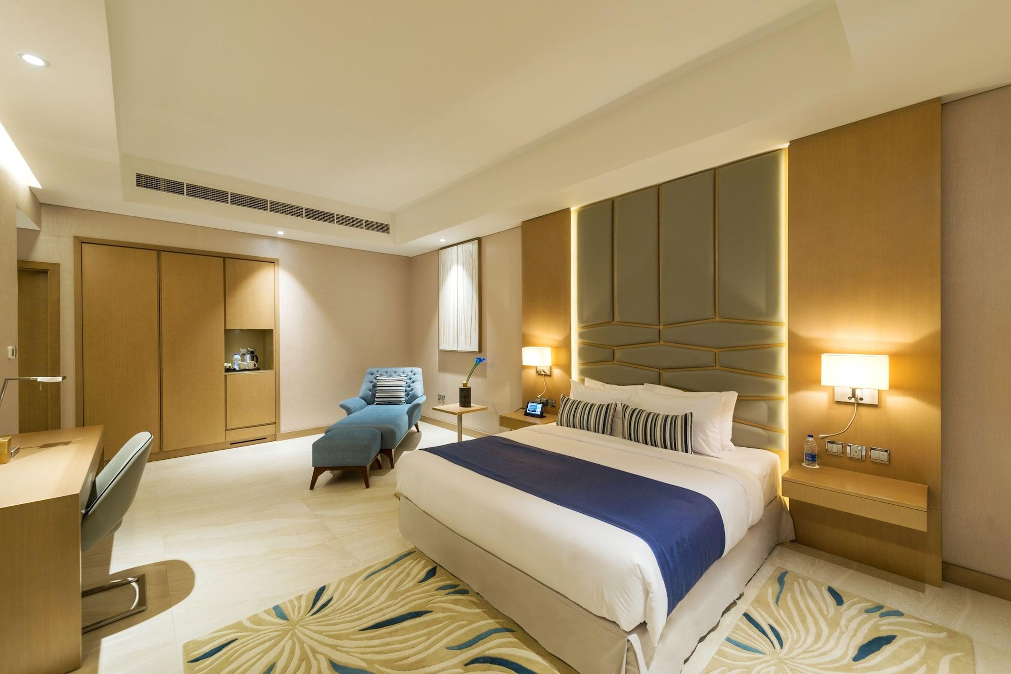 Canal Central Hotel Business Bay Dubaj Zewnętrze zdjęcie The photo shows a modern hotel room that appears to be well-designed and spacious. In the center, there is a comfortable bed with white linens and a blue accent blanket. A stylish headboard complements the bed. To the side, there is a lounge chair in