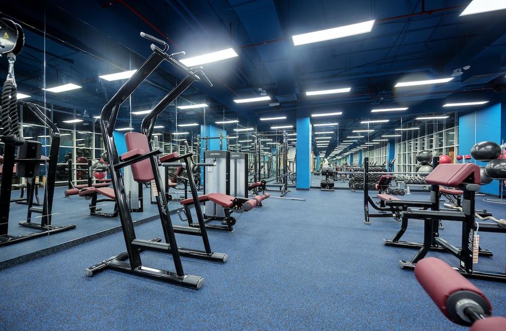 Canal Central Hotel Business Bay Dubaj Zewnętrze zdjęcie The photo shows a gym interior with various exercise equipment. There are machines designed for strength training, including a multi-station machine and benches. The floors are covered with blue carpet, and there are large mirrors on the walls, refle