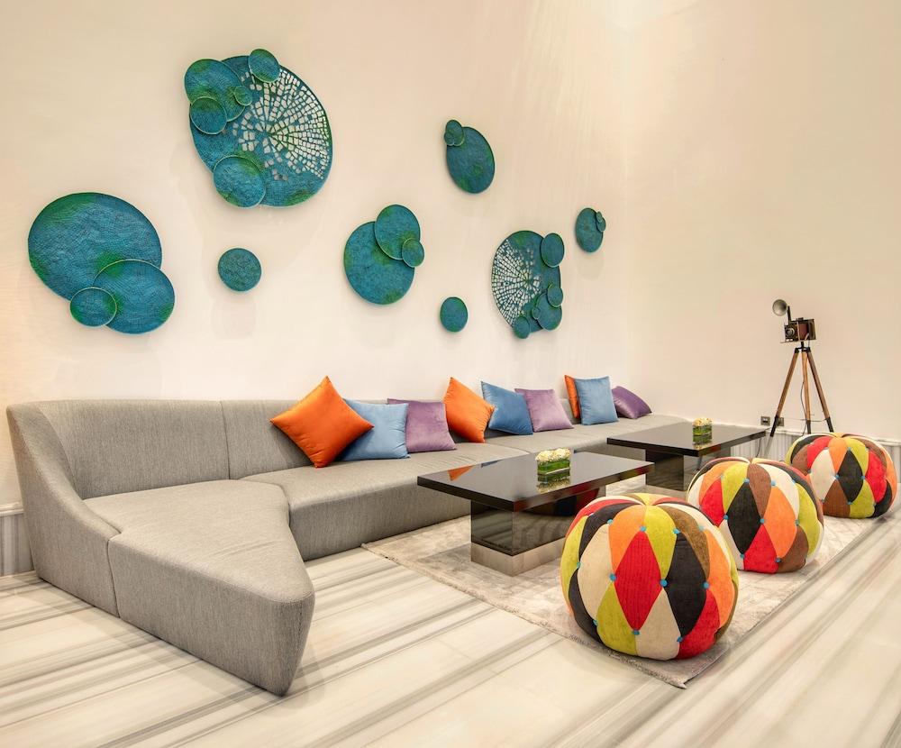 Canal Central Hotel Business Bay Dubaj Zewnętrze zdjęcie The photo depicts a modern and stylish lounge area. There is a grey, curved sofa adorned with colorful throw pillows in shades of orange, purple, and blue. In front of the sofa, there are two sleek coffee tables. The wall behind is decorated with art