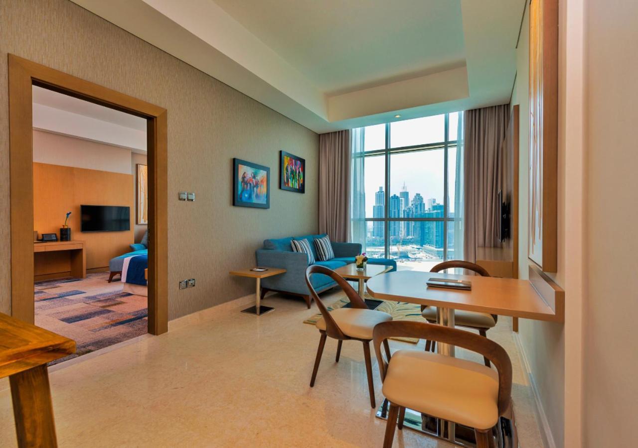 Canal Central Hotel Business Bay Dubaj Zewnętrze zdjęcie The photo shows a modern interior space, likely a living area or suite. On one side, there’s a small dining table with chairs, and on the other, a comfortable couch positioned near large windows that allow natural light to fill the room. The walls ar