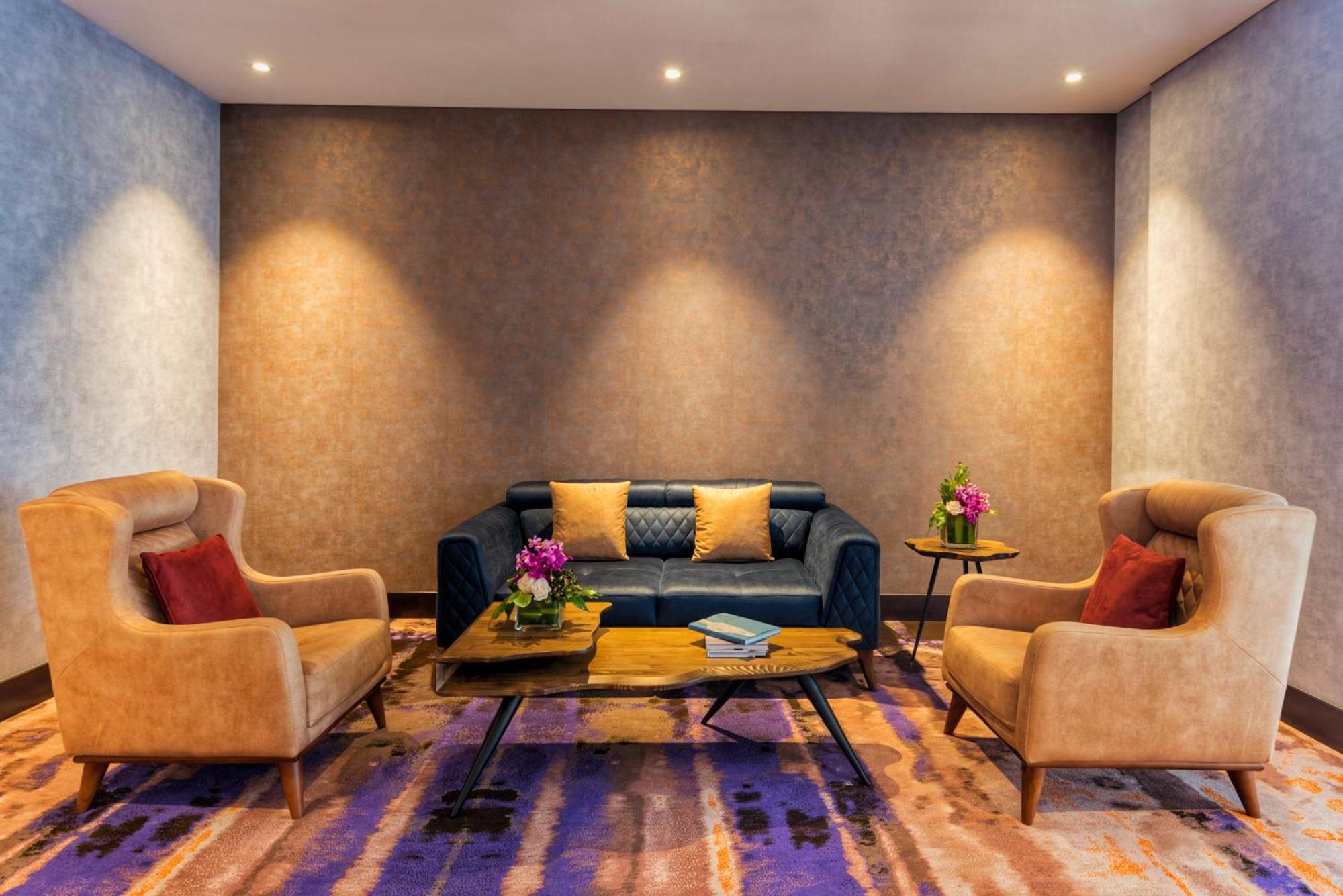 Canal Central Hotel Business Bay Dubaj Zewnętrze zdjęcie The photo shows a cozy and stylish seating area. There is a dark blue sofa in the center, accented with colorful cushions. On either side of the sofa, there are two beige armchairs, each with red cushions. A wooden coffee table sits in front of the s