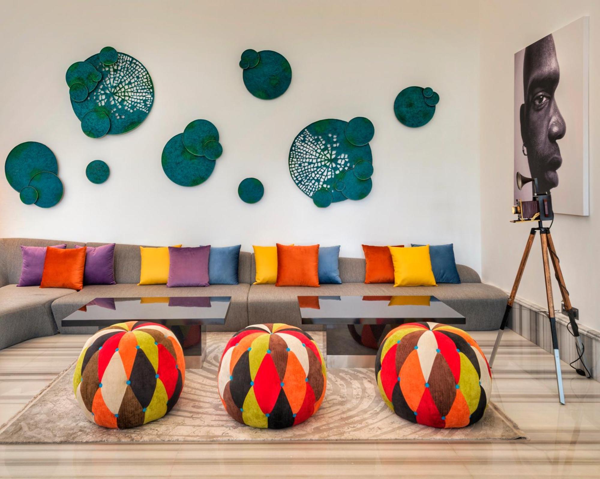 Canal Central Hotel Business Bay Dubaj Zewnętrze zdjęcie The photo shows a modern living space with a contemporary design. There is a comfortable gray sofa adorned with colorful cushions in various shades of orange, purple, and yellow. In front of the sofa, there are round ottomans or poufs with a vibrant 