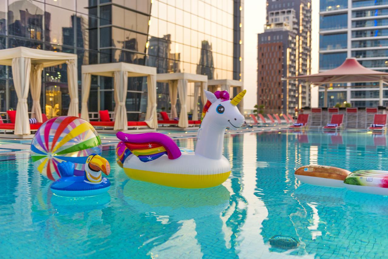 Canal Central Hotel Business Bay Dubaj Zewnętrze zdjęcie The photo shows a swimming pool with colorful inflatable pool toys. There is a large inflatable unicorn, which is white with a rainbow mane and a golden horn. Nearby, there is a smaller inflatable in the shape of a turtle. Another floating toy resemb