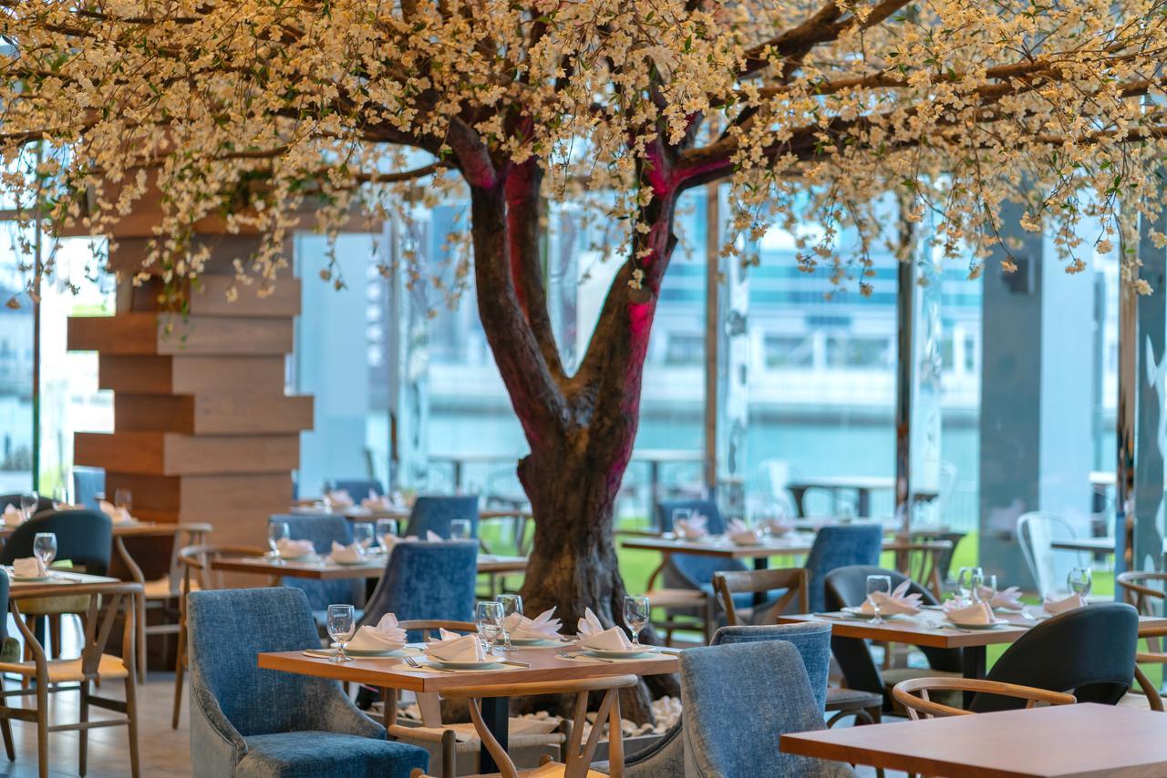 Canal Central Hotel Business Bay Dubaj Zewnętrze zdjęcie The photo depicts an elegantly designed restaurant interior featuring a large, decorative tree in the center. The tree has a thick trunk and branches adorned with delicate, white flowers, creating a charming and inviting atmosphere. Surrounding the t