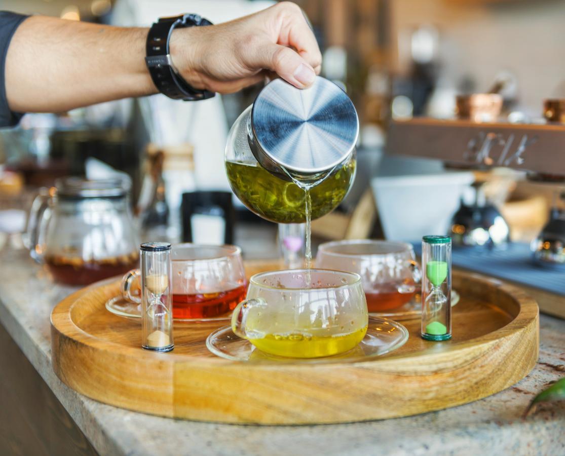 Canal Central Hotel Business Bay Dubaj Zewnętrze zdjęcie The photo shows a person pouring a liquid from a metallic container into a glass teacup. There are several glass teacups arranged on a wooden tray, each containing different colored liquids, likely various types of tea. Next to the cups, there are sm