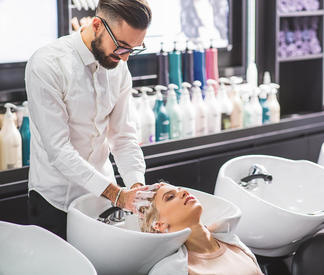 Canal Central Hotel Business Bay Dubaj Zewnętrze zdjęcie The photo shows a hair salon setting where a stylist is washing a client's hair. The stylist, dressed in a white shirt, is standing behind a sink, gently massaging shampoo into the client's hair. The client is reclined back, enjoying the process. In 